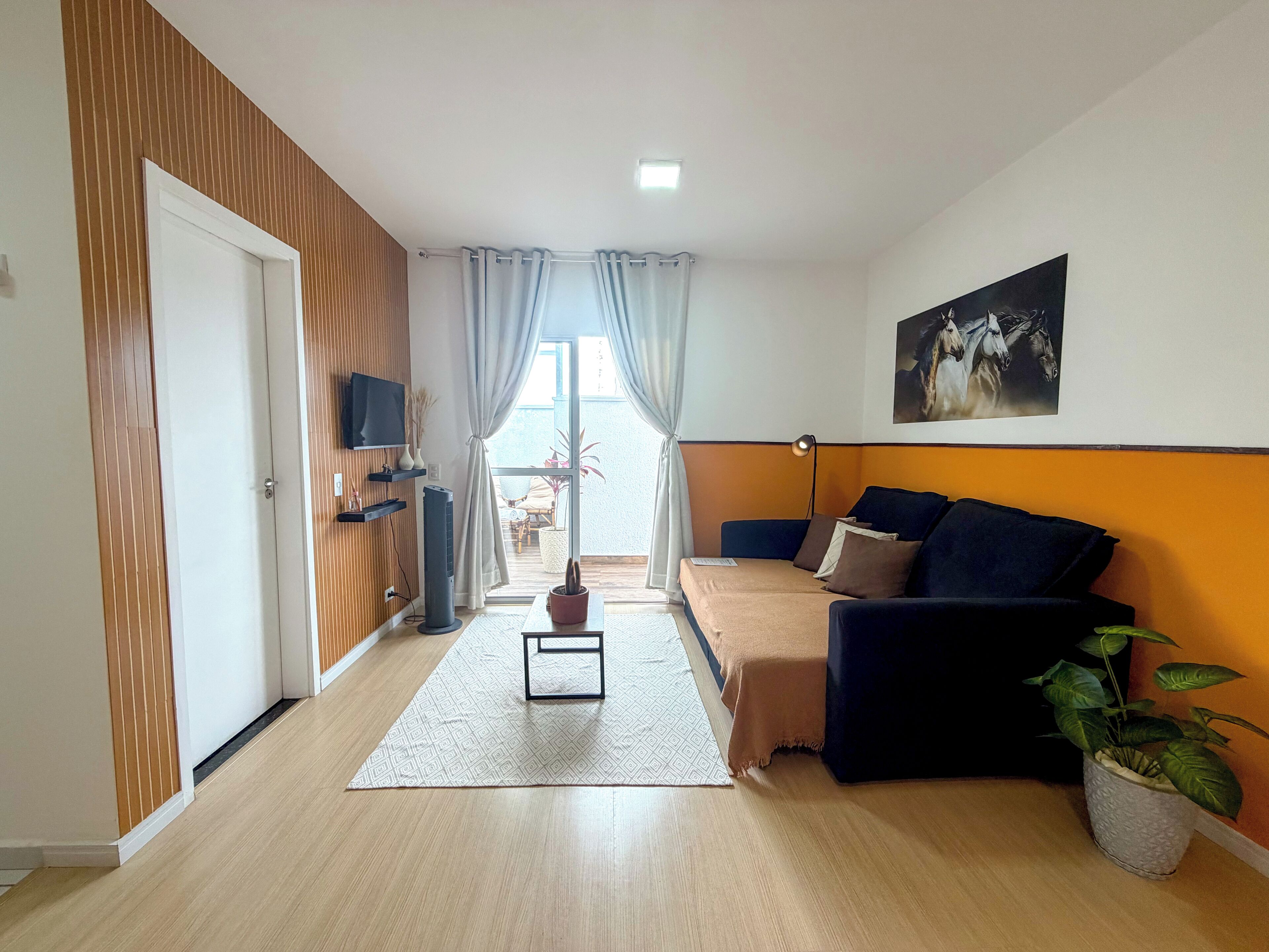 A modern living room with a sofa, a flat-screen TV, a potted plant, and a view to the outside.