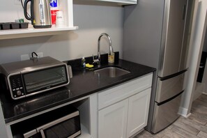A compact kitchen with a microwave, a sink, and a stainless steel refrigerator.