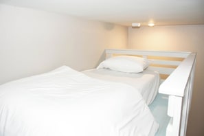A single bed with white bedding in a room with plain walls and a ceiling light.