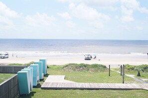 A beach view with a wooden boardwalk leading to beachside seating, a sandy beach, and the ocean in the background.