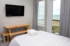 A bedroom with a bed, a wooden desk, a television, and a window with a view of the sea.