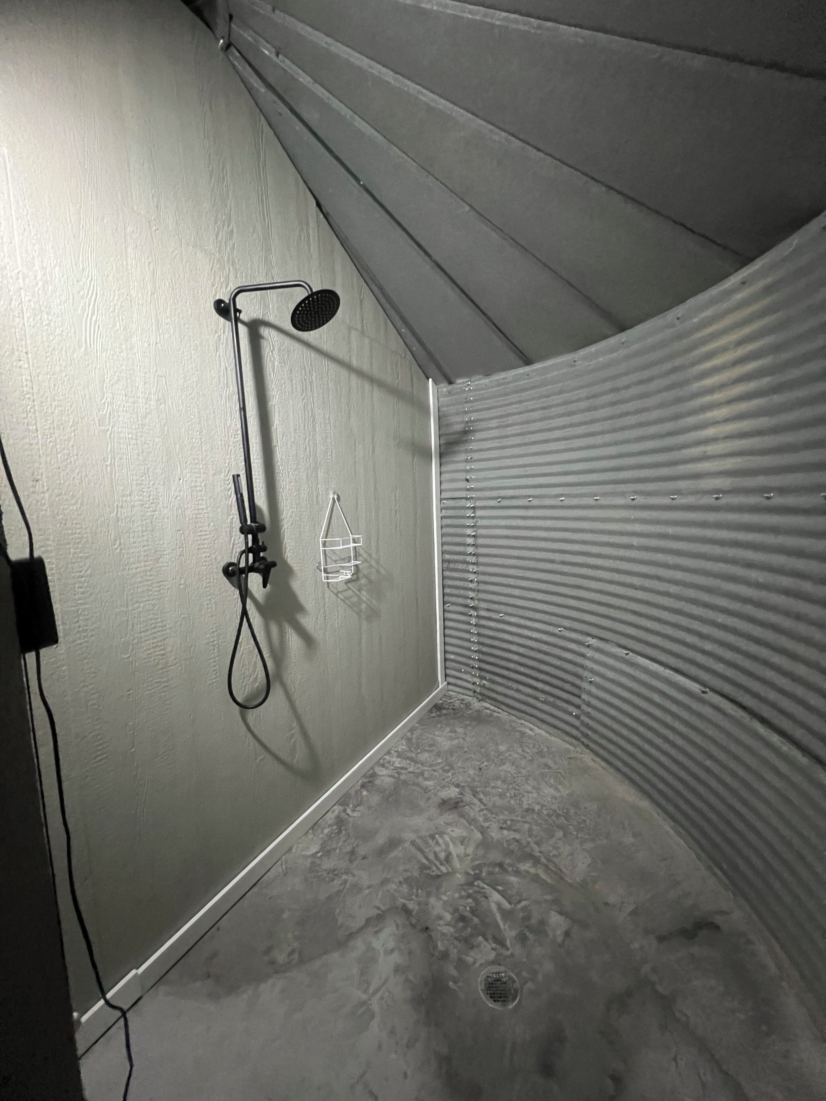 A corner of a room with a shower, a drain, and a wall-mounted towel rack.