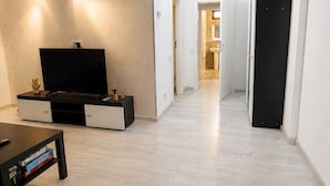 Una sala de estar moderna con un televisor de pantalla plana, una mesa de centro con libros y un pasillo que da a una cocina.