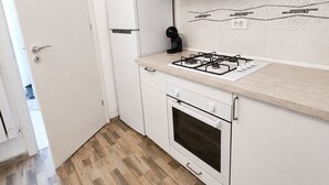 Una cocina con armarios blancos, estufa a gas, horno empotrado y refrigerador.
