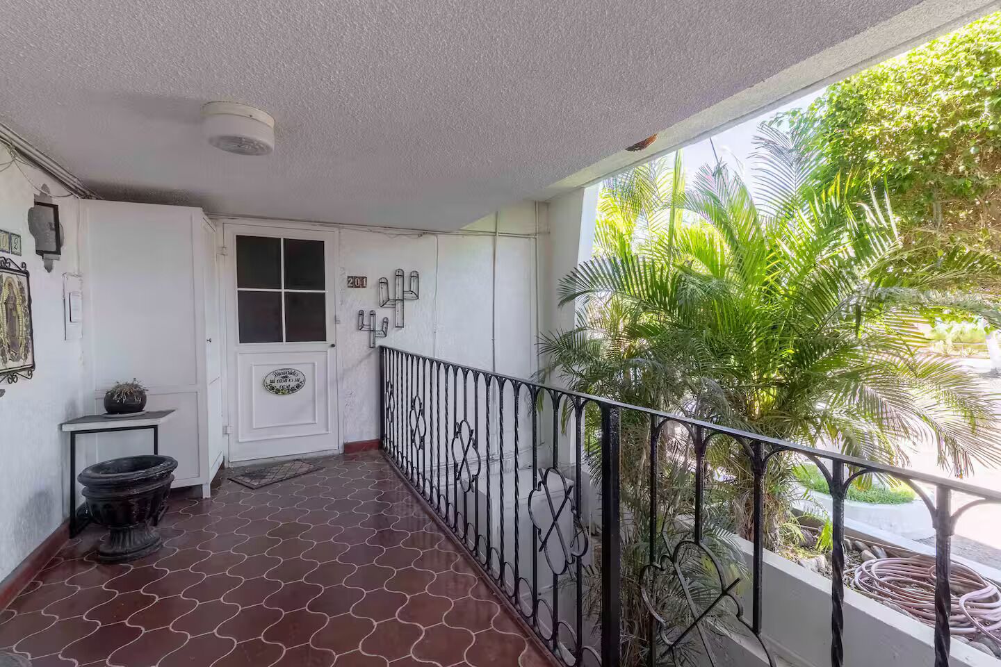 Un balcón con piso estampado, una puerta blanca y barandilla de metal.