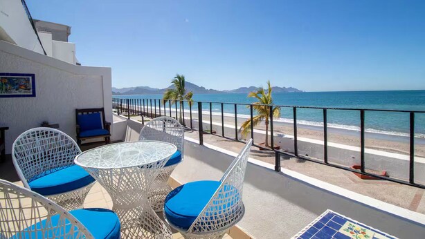 Un balcon avec une table et des chaises, donnant sur une plage et la mer.
