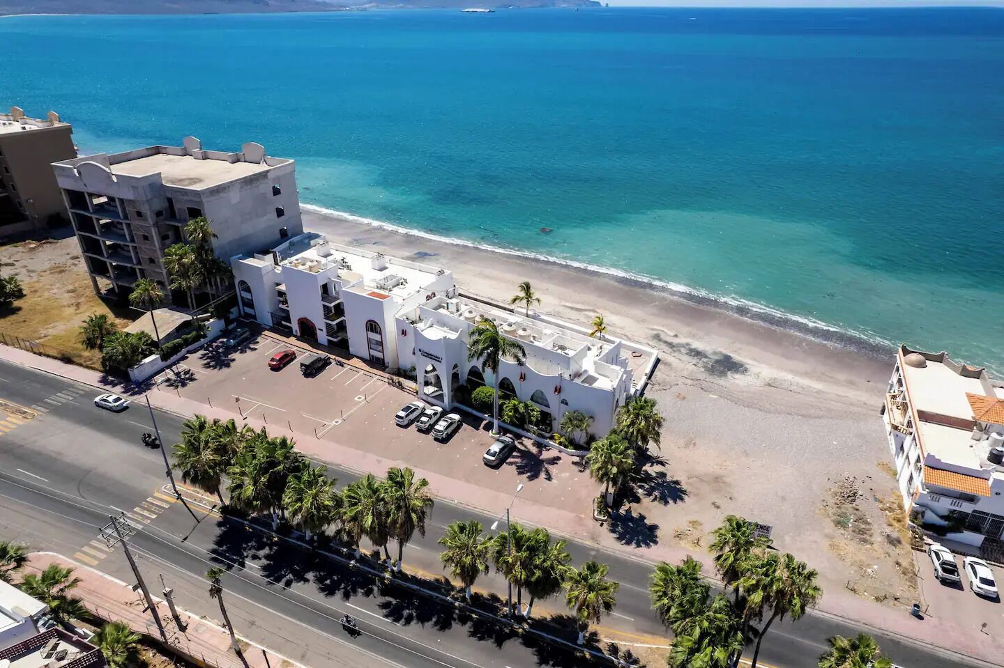 Ein Küstenhotel mit Parkplatz, Blick auf den Strand und einer Straße im Vordergrund.