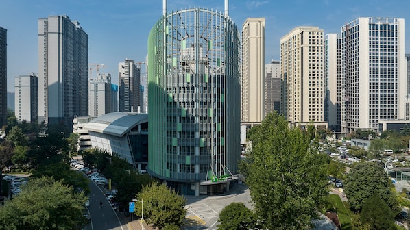 A modern high-rise building with a unique cylindrical structure, surrounded by other tall buildings and a parking area. - Holiday Inn Express Xi'an Qujiang Center (Xi'an)