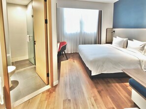 Ein Hotelzimmer mit Bett, Nachttisch, Stuhl und einem Badezimmer mit Toilette und Dusche.