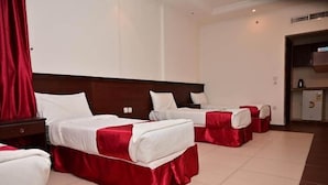 Une chambre d’hôtel avec trois lits, chacun recouvert d’une courtepointe rouge et blanche, et un petit coin cuisine.