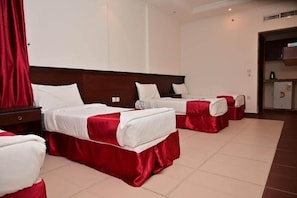 Ein Hotelzimmer mit drei Betten, jedes mit einer rot-weißen Tagesdecke, sowie einer kleinen Küchenzeile.