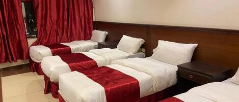 A hotel room with four single beds arranged in a row, each with a red and white bedspread.