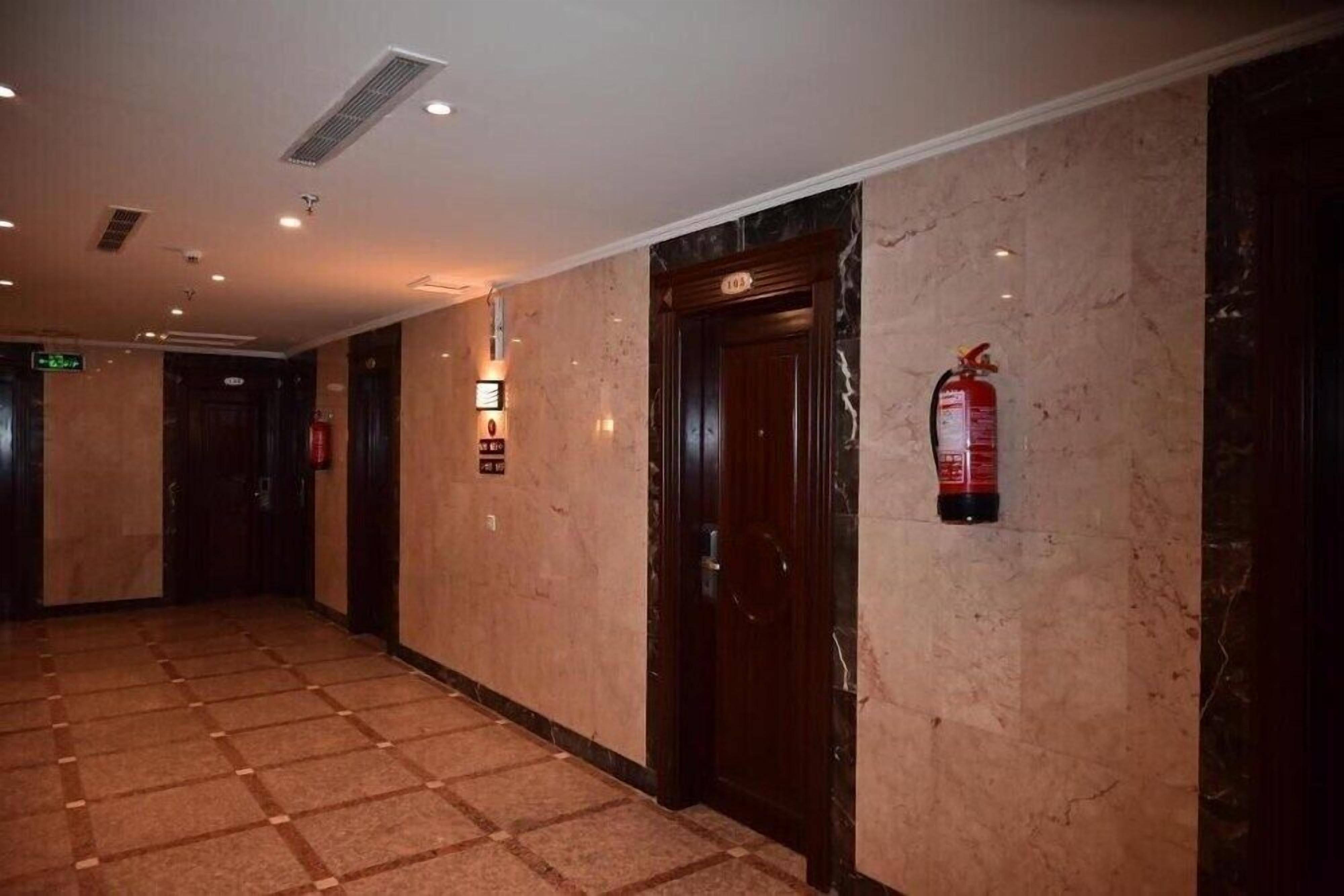 A hallway with marble walls, a fire extinguisher mounted on the wall, and a door with a number plate.