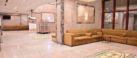A lobby with a marble floor, a large beige sofa, and a glass wall.
