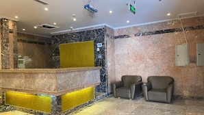 Un hall d’entrée avec un comptoir de réception, deux fauteuils et un panneau de séparation jaune.