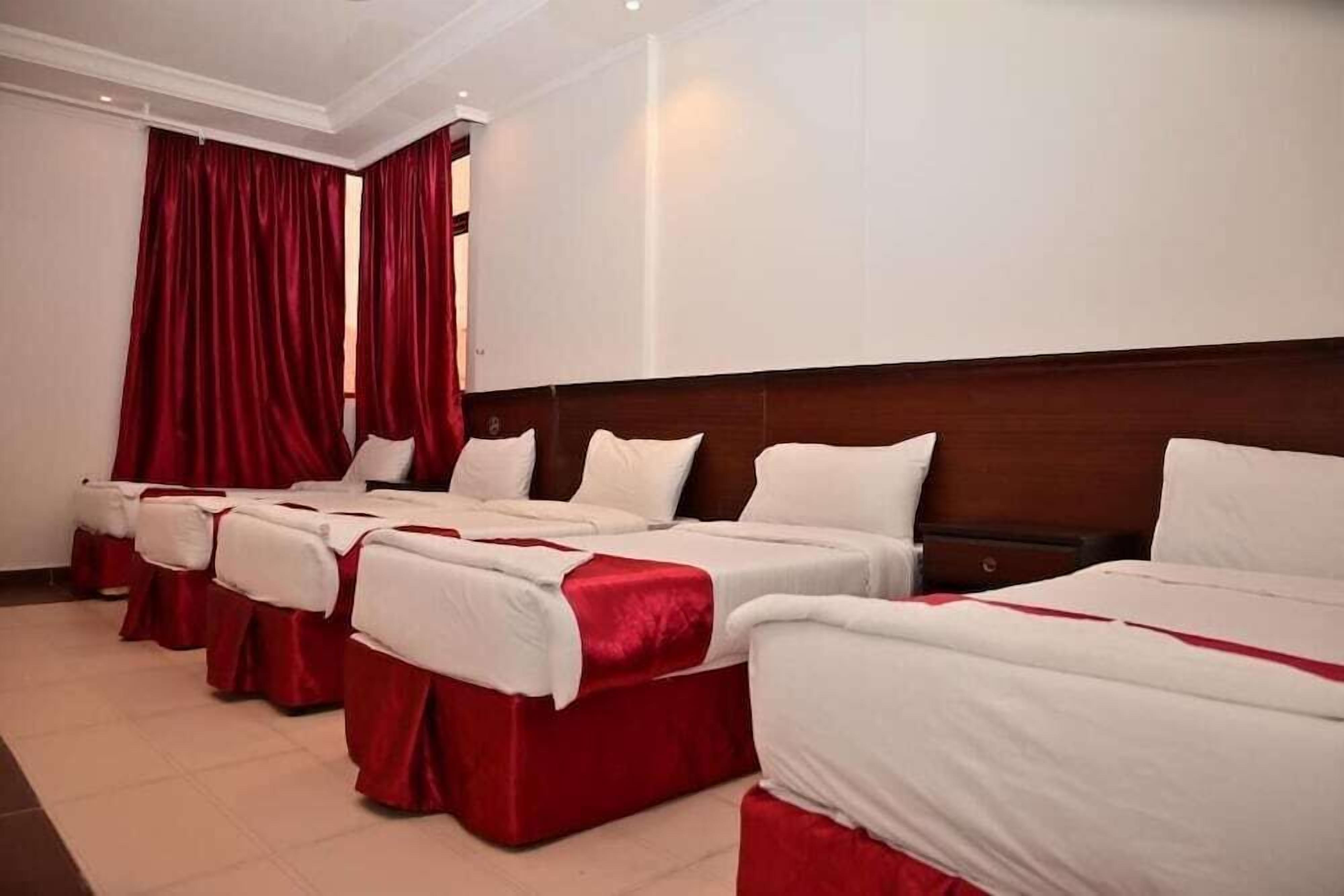 Une chambre d’hôtel avec quatre lits alignés, chacun étant doté de draps blancs et de touches de couleur rouge.