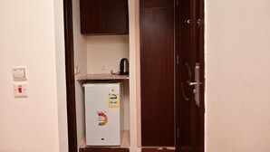 Une pièce de taille modeste, équipée d’un petit réfrigérateur, d’une porte en bois et d’un interrupteur fixé au mur.