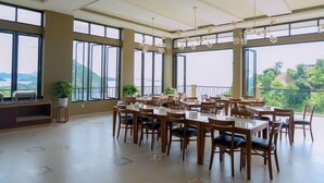 A spacious dining area with multiple tables and chairs, large windows offering a view of the outdoors, and a ceiling with hanging light fixtures. - Flamingo Waecicu Labuan Bajo (Labuan Bajo)