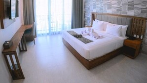 A hotel room with a large bed, a wooden nightstand, a desk, and a large window with curtains. - Flamingo Waecicu Labuan Bajo (Labuan Bajo)