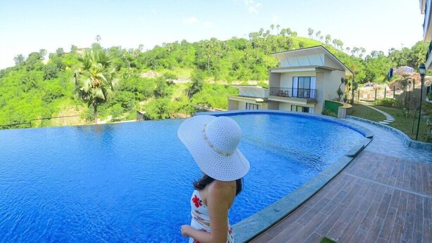 A person standing by a swimming pool with a view of a hillside and a building in the background. - Flamingo Waecicu Labuan Bajo (Labuan Bajo)