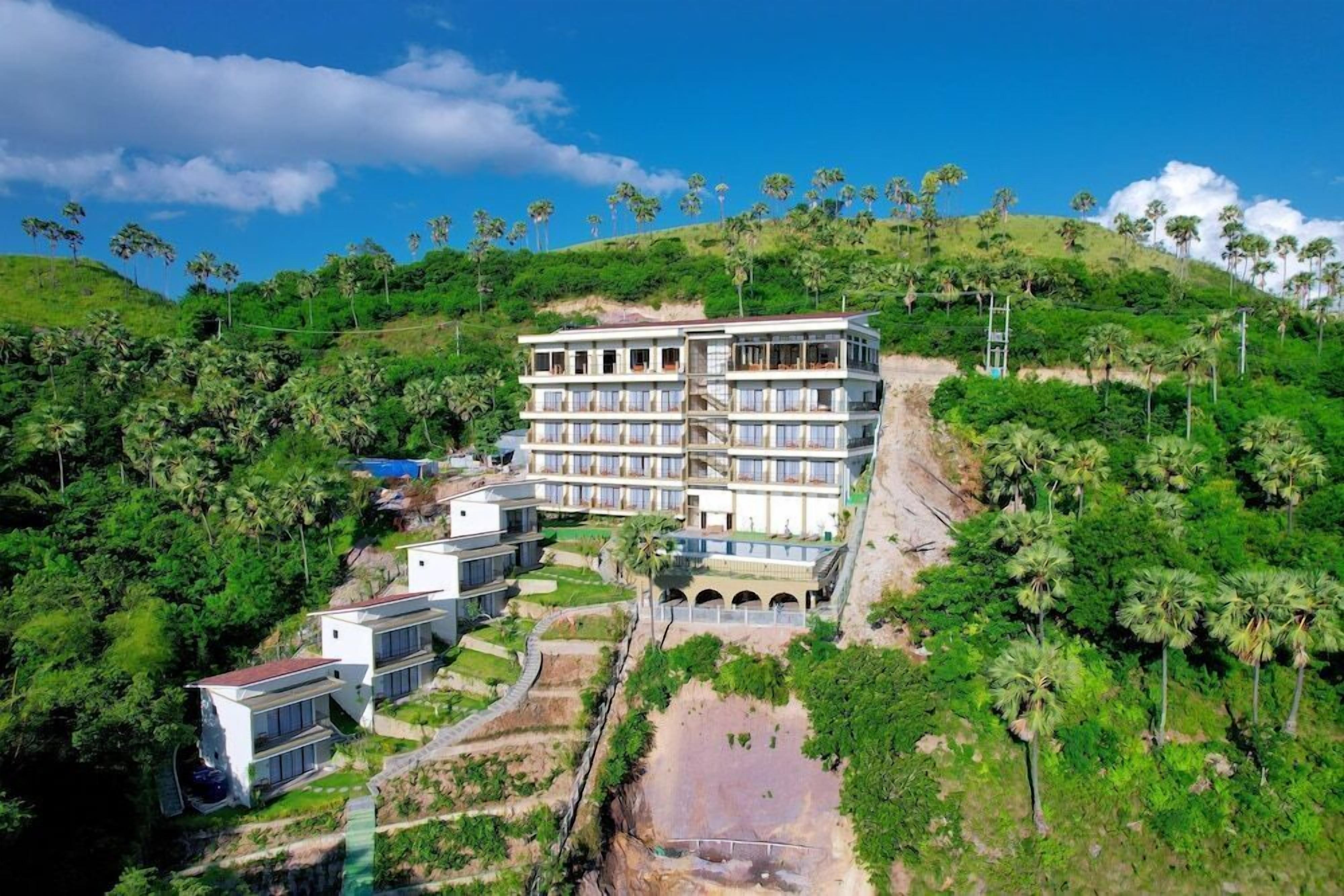 A multi-story hotel with a pool and lush greenery surrounding it.