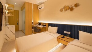 Ett hotellrum med två sängar, ett skrivbord, en stol, en garderob och en luftkonditioneringsanläggning.