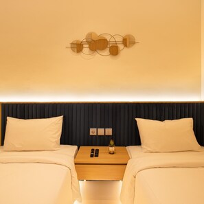 A hotel room with two beds, a nightstand, and a wall-mounted light fixture. - The Risman Hotel At Jakarta Airport CBC (Tangerang)