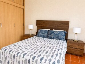 Un dormitori amb un llit, dues taules de nit, un armari de fusta i un estri de llit estampat.