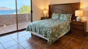 Quarto com cama, duas mesas de cabeceira, um criado-mudo, uma janela grande e vista para o mar.