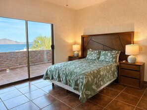Ein Schlafzimmer mit einem Bett, zwei Nachttischen, einem Fenster mit Blick auf das Meer.