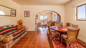 Uma sala de estar com sofá, uma mesa de jantar com cadeiras, lareira e vista através de um arco.