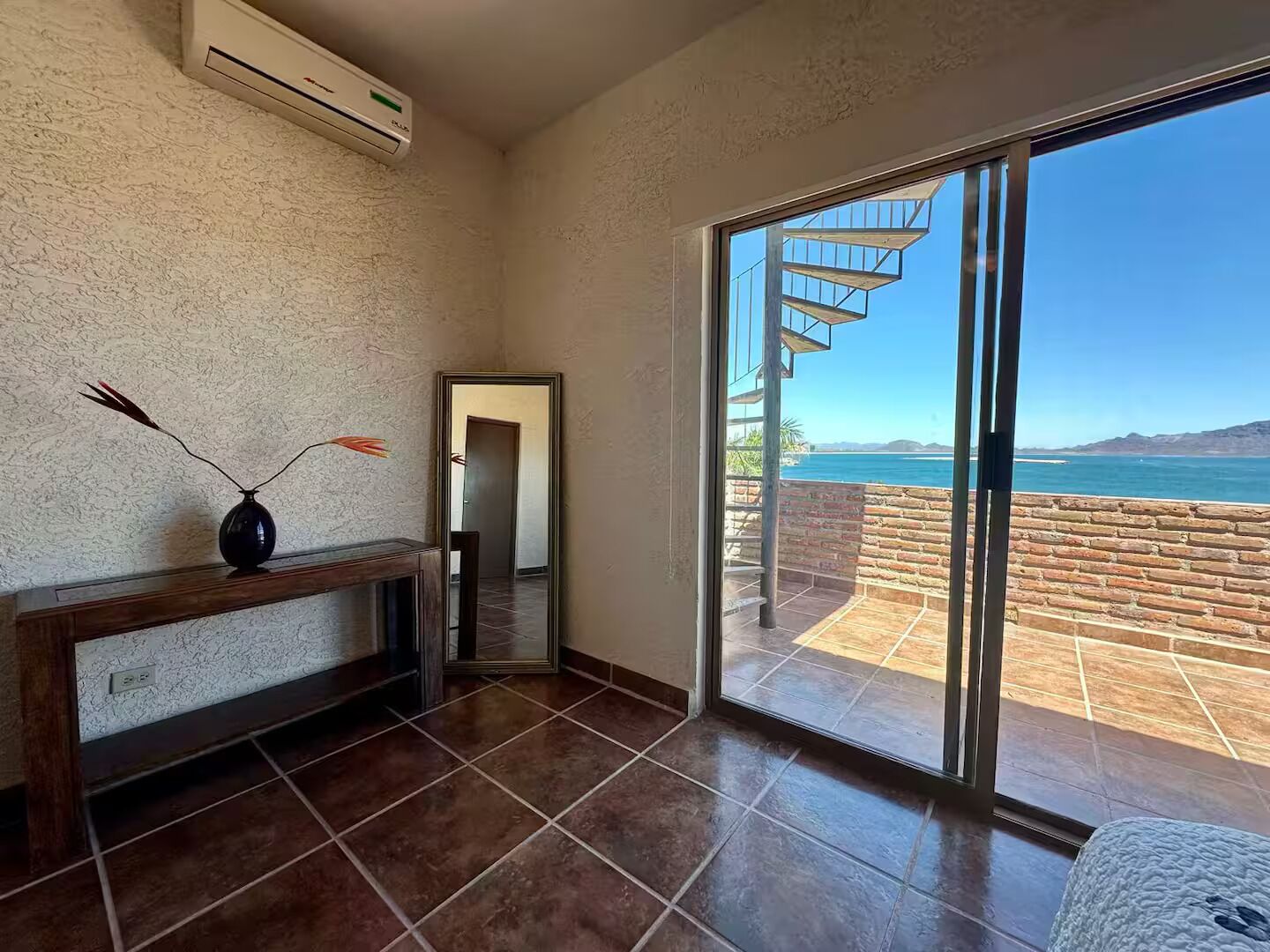 A room with a large sliding glass door leading to a balcony with a view of the sea.