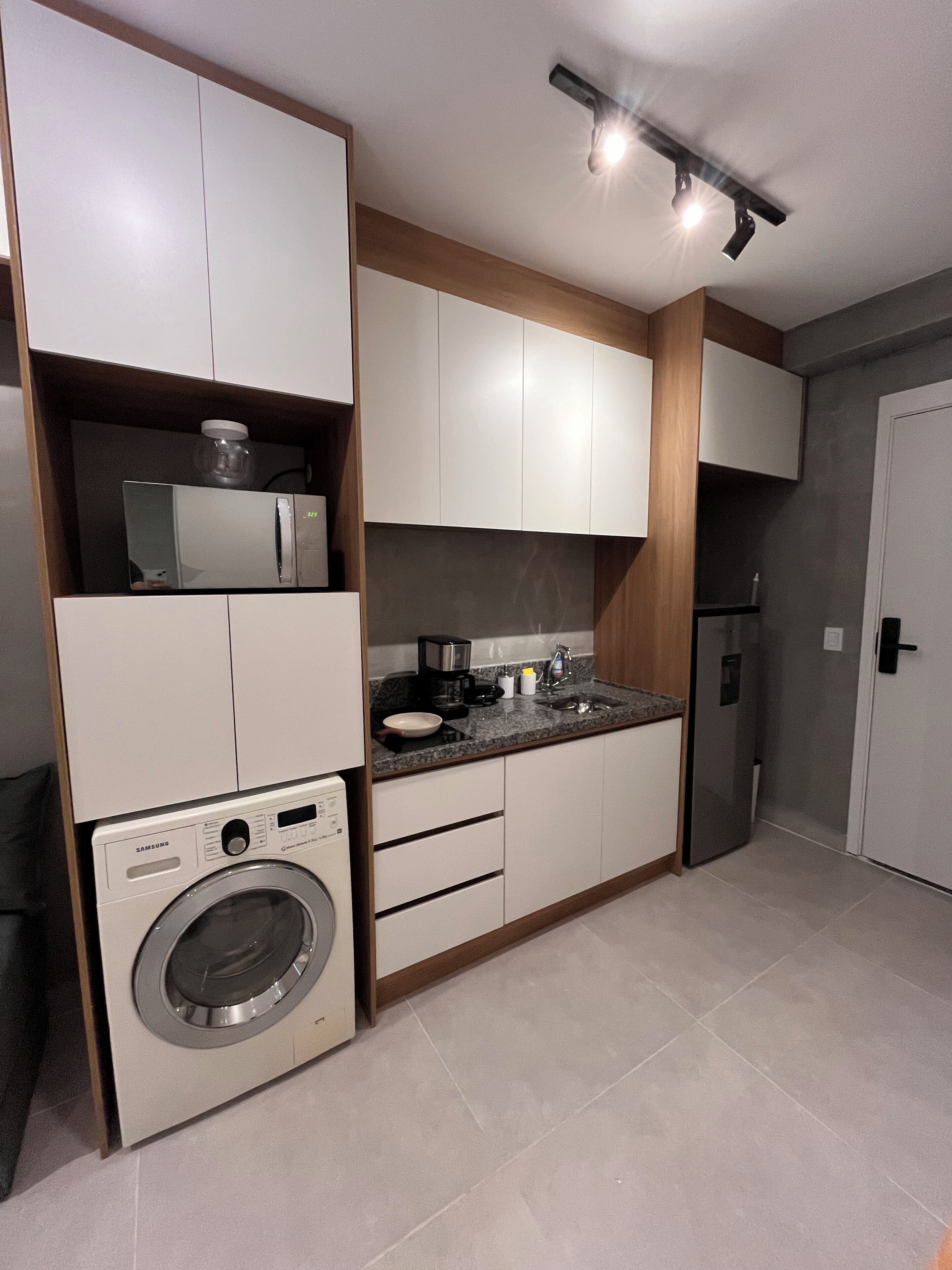 Une cuisine compacte dotée d’appareils électroménagers intégrés, notamment un four à micro-ondes, une machine à café et un lave-linge.