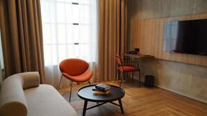 Un soggiorno moderno con un divano, un tavolino rotondo con libri, una poltrona rossa, una TV montata a parete e un pavimento in legno.