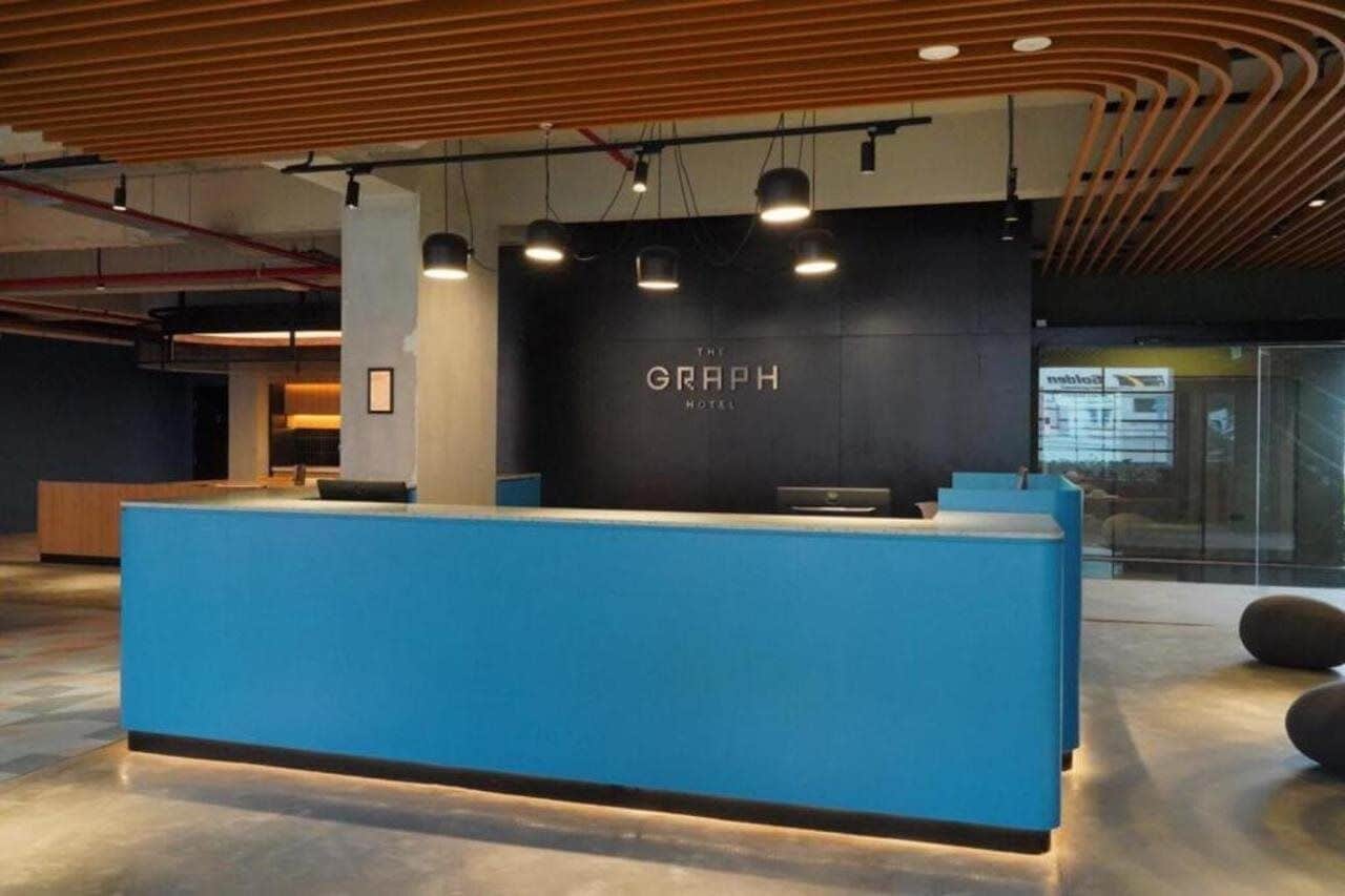 A reception desk with a blue counter and a black wall with the text 'THE GRAPH HOTEL'.