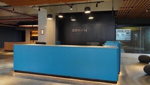 Una reception con un bancone blu e una parete nera con la scritta 'THE GRAPH HOTEL'.