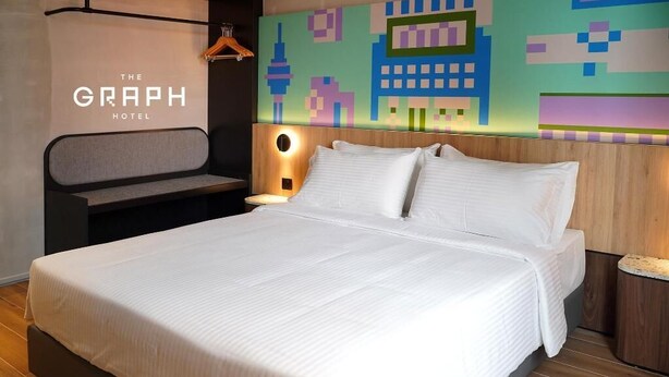 Una camera d'hotel con un letto grande, una testiera luminosa integrata e un colorato murale.
