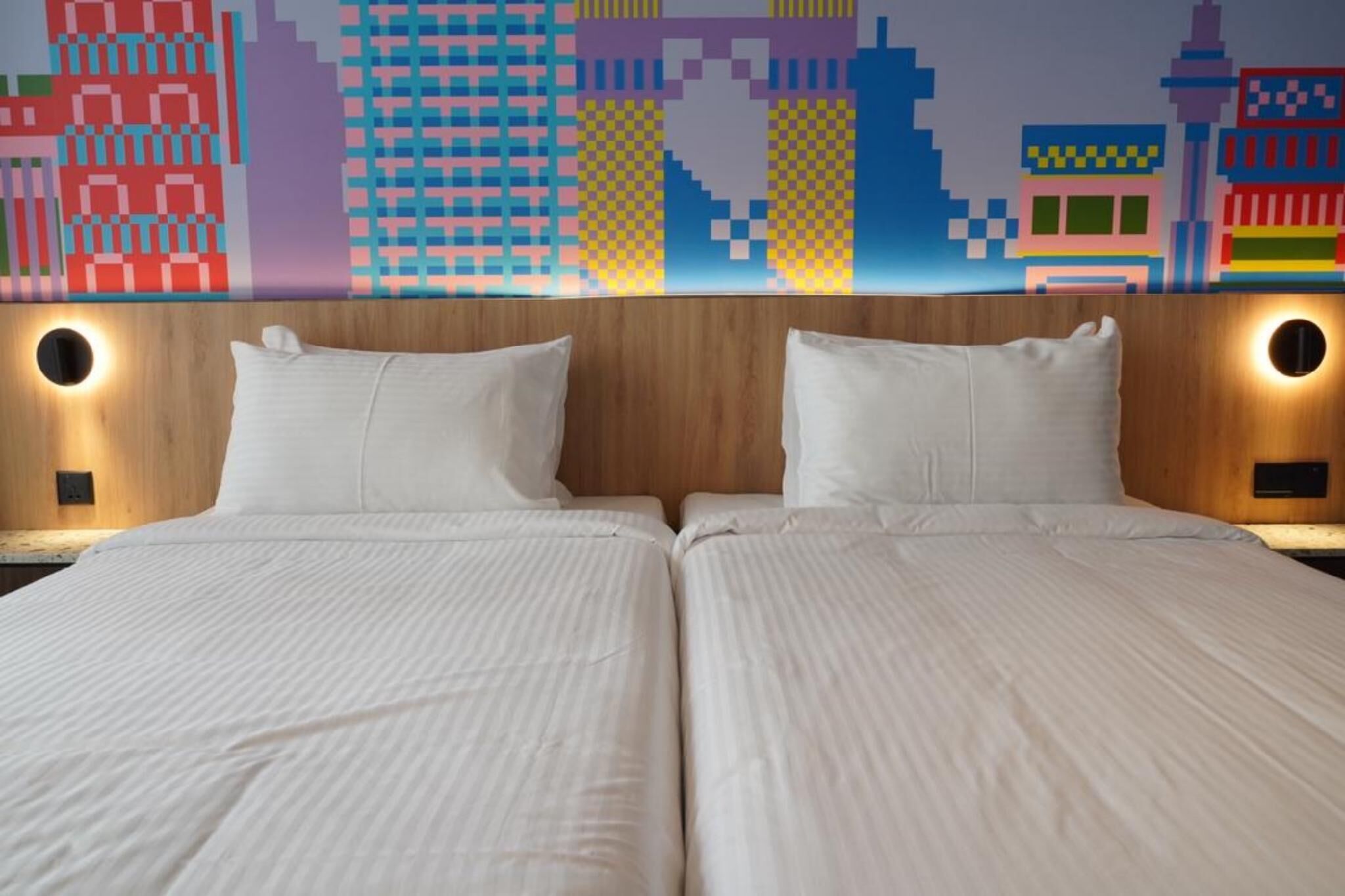 A double bed with a cityscape mural on the wall behind it.