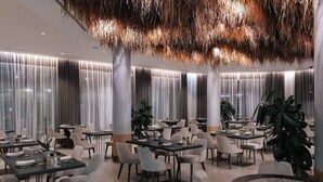 Un'area ristorazione moderna con diversi tavoli e sedie, una pianta al centro e un design di soffitto originale.