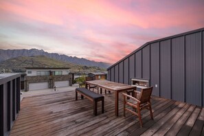 A deck with a wooden table and chairs, a bench, and a fireplace. - Highview Vista - Lake views, Outdoor Fireplace, great for families (Queenstown)