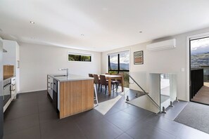 A modern kitchen with a central island, dining area with chairs, and a view of the outdoors. - Highview Vista - Lake views, Outdoor Fireplace, great for families (Queenstown)