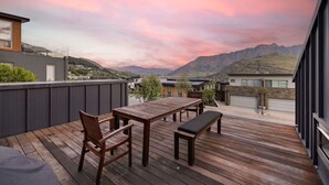 Um deck de madeira com mesa e cadeiras, com vista para uma paisagem montanhosa.