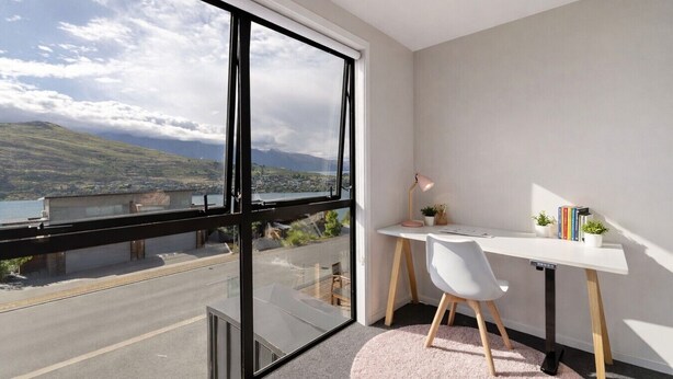 Quarto moderno com uma grande janela, uma escrivaninha, uma cadeira e vista para a paisagem costeira.