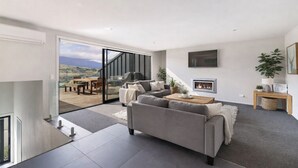 Uma sala de estar moderna com um sofá cinza, uma lareira e uma janela grande com vista para um deck.