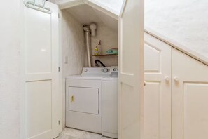 Un lavadero con lavadora y secadora, conducto de ventilación y estante con productos de limpieza.