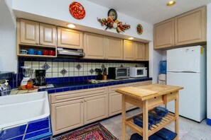 Una cocina con armarios color beige, un salpicadero de azulejos azules, una mesa de madera y un refrigerador.