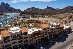 Un pueblo costero con un puerto deportivo, edificios con tejados rojos y terreno montañoso al fondo.