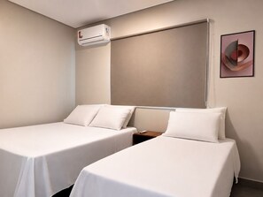 A hotel room with two single beds, a wall-mounted air conditioner, and a framed abstract artwork.