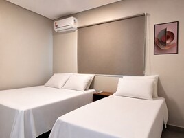 Habitación de hotel con dos camas individuales, aire acondicionado instalado en la pared y una obra de arte abstracta enmarcada.