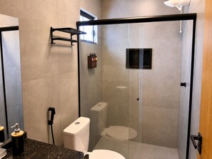 A modern bathroom with a glass-enclosed shower, a toilet, and a sink with a soap dispenser.